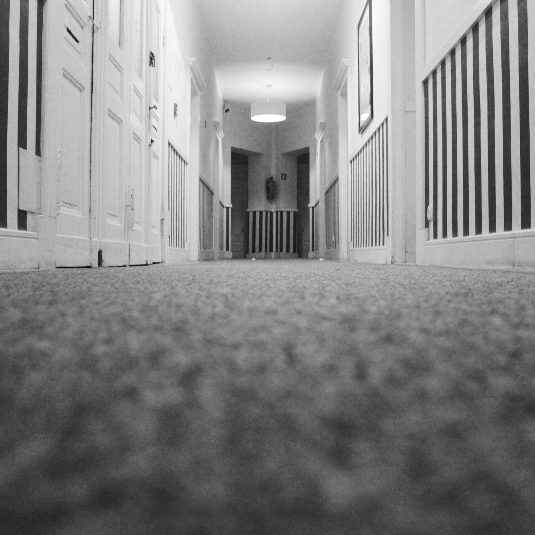 Low angle view of an empty hotel corridor with striped walls and carpet in monochrome.