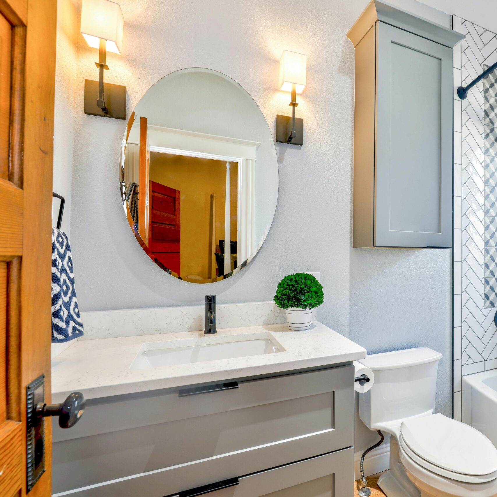Elegant modern bathroom featuring chevron tiles, oval mirror, and sleek fixtures for a contemporary look.